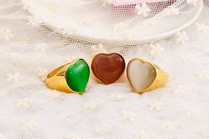Macro shot of three gold heart rings with green, brown and cream gemstones on lace