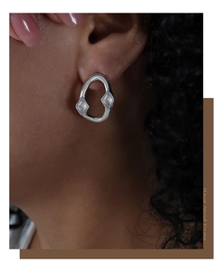 Macro shot of silver irregular hoop earring with rhombus zircon on female model's ear
