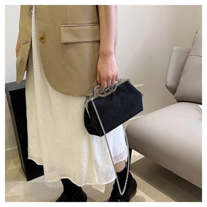 Elegante pochette nera con strass e catena argentata, indossata su un raffinato abito beige