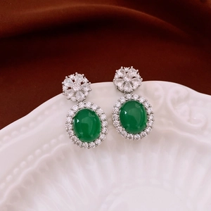 Detail of vintage emerald green oval earrings with micro-set diamonds on a white ceramic plate