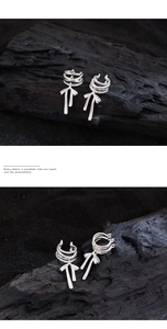 Close-up of silver ribbon bow ear clips with tassel fringe on a textured dark background