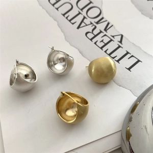 Macro shot of minimalist brushed silver and gold metal ball earrings on paper