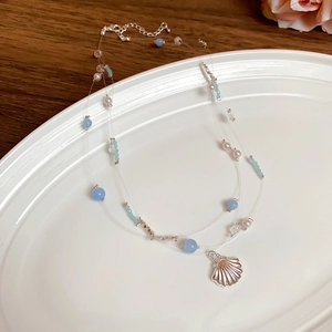 Multi-layer beach necklace with blue beads and silver shell pendant on white plate