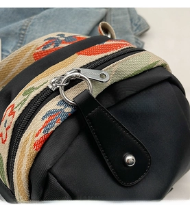 Macro shot of smooth metal zipper and ethnic woven strap on a black nylon crossbody bag