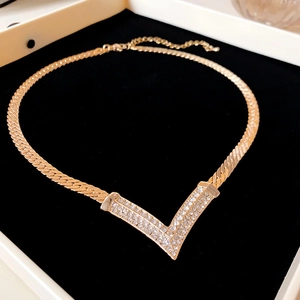 Detailed view of a gold snake chain necklace with a V-shaped rhinestone pendant on velvet