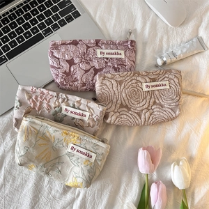 Flat lay of french floral embossed toiletry bags on soft bedding with home decor