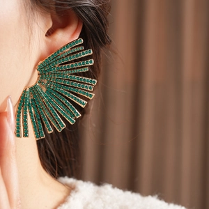 Detailed shot of large gold fan earrings featuring emerald green rhinestones on model