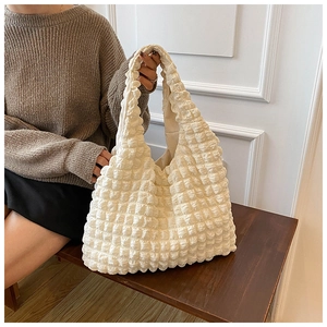 Close-up of cream white shoulder bag featuring unique bubble textured fabric on wooden bench