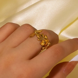 Polished gold floral ring with adjustable band shown on hand against silk fabric