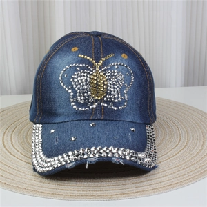 Détails des motifs papillons en strass et clous métalliques sur casquette en jean bleu