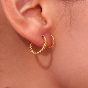 Macro detail of 18K gold plated twisted and smooth hoop earrings worn on a model ear