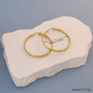 Detail shot of golden 4cm hoop earrings on stone platform with size and weight info