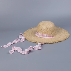 Detail of pink plaid ribbon on raffia straw sun hat with frayed edge and woven texture