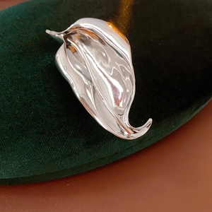 Macro shot of silver leaf brooch with polished metallic texture on green velvet background
