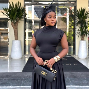 Detail of elegant black sleeveless midi dress with chic mesh hat and gold handle handbag