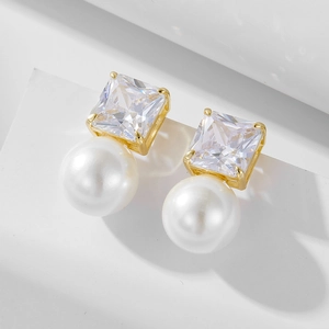 Macro view of square-cut zircon and white pearl stud earrings with gold plating
