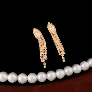 Detailed view of gold fringe earrings with zircon inlay on a black velvet background