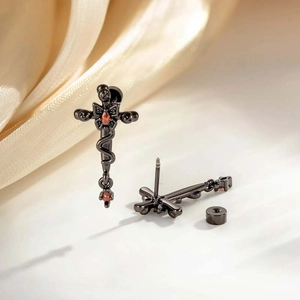 Black cross stud earrings with red gemstones on gold silk fabric in a macro view