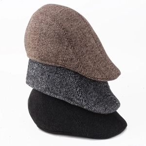 Stack of wool blend newsboy caps showing herringbone pattern in brown, grey and black