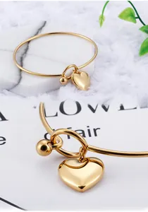 Macro detail of a gold heart pendant and T-bar toggle clasp on a minimalist bangle