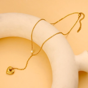 Golden heart necklace with a single pearl pendant on a minimal display stand