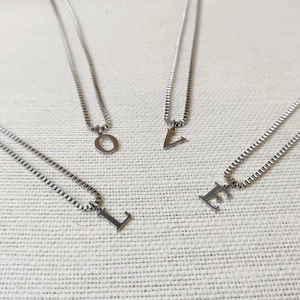 Detail shot of four silver stainless steel initial necklaces spelling LOVE on white fabric
