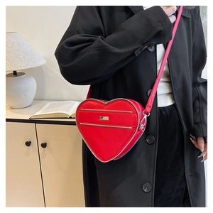 Detail view of a red heart-shaped leather crossbody bag with silver zipper and slim strap
