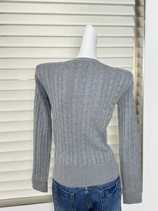 Rear view of grey cable-knit sweater with ribbed cuffs on a mannequin with blue jeans