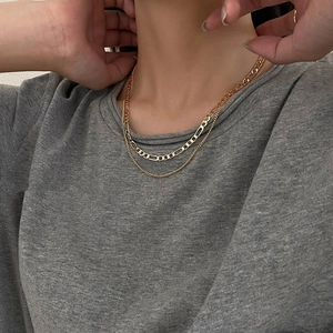 Detail of layered gold Figaro necklace worn by model showing textured chain links