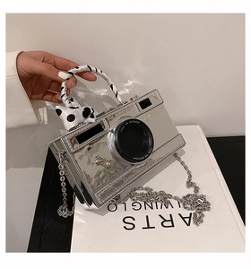 Macro view of silver camera-shaped handbag with silk ribbon and metal chain strap