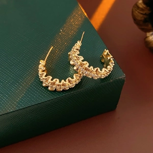 Macro shot of 18k gold plated wave earrings with zircon stones on green textured surface