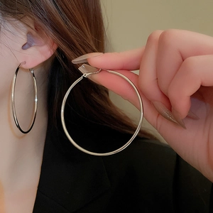 Close-up of a model wearing large polished silver hoop earrings with a minimalist design