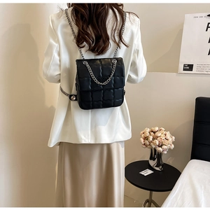Rear view of a model wearing a black quilted leather backpack with silver chain straps