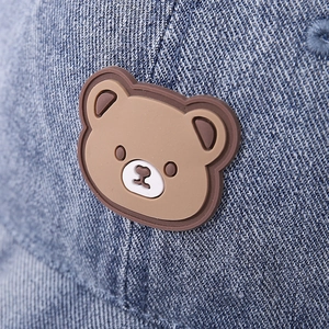 Detail of blue denim baby cap featuring a 3D brown bear silicone patch on washed fabric