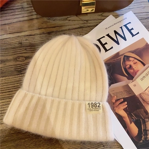 Detail shot of a soft cream knitted beanie with 1982 California label on wood table