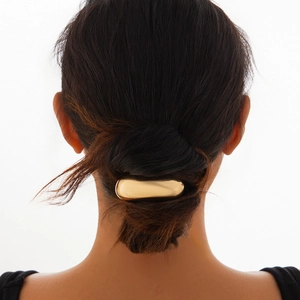 Detail view of a minimalist gold oval hair tie accessory on a woman's hair bun
