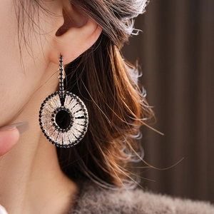 Close-up of gold geometric hoop earrings with blue and white zircon stones on a model