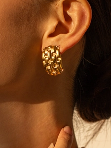 Close-up of gold-plated wide textured hoop earrings with woven pattern on model's ear