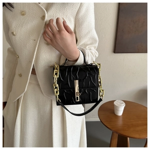 Detail of black textured handbag with gold chain strap held by model in tweed suit