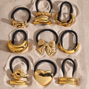 Set of nine golden stainless steel hair rings with diverse metal designs on sand background