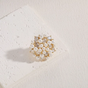 Detail of gold evil eye brooch with white pearl and clear zircon on textured surface