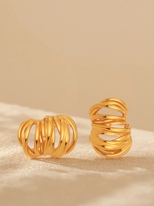 Macro shot of gold-plated stainless steel multi-layered spiral hoop earrings on sand