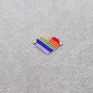 Detail of a handmade rainbow heart charm made of Miyuki seed beads on gray felt