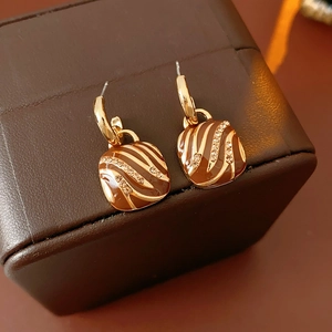 Detailed view of gold square drop earrings with brown enamel swirls and sparkling crystals