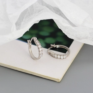 Macro shot of silver S925 geometric hoop earrings with diamonds on white paper