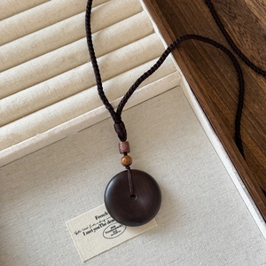 Detalle de colgante de madera nube de la suerte en collar de cordón trenzado vintage