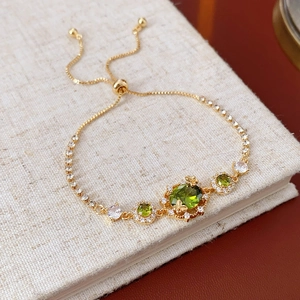 Détail d'un bracelet plaqué or avec des pierres précieuses vertes et motif de papillon