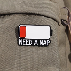 Detail of NEED A NAP battery enamel pin attached to olive green canvas fabric