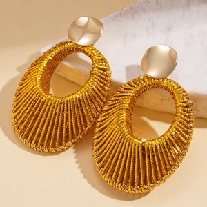 Detailed view of gold woven oval hoop earrings with circular metal studs on marble base