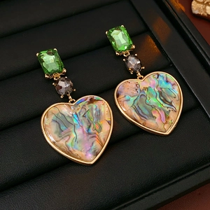 Close-up of vintage heart earrings with green gems and abalone shell on jewelry tray